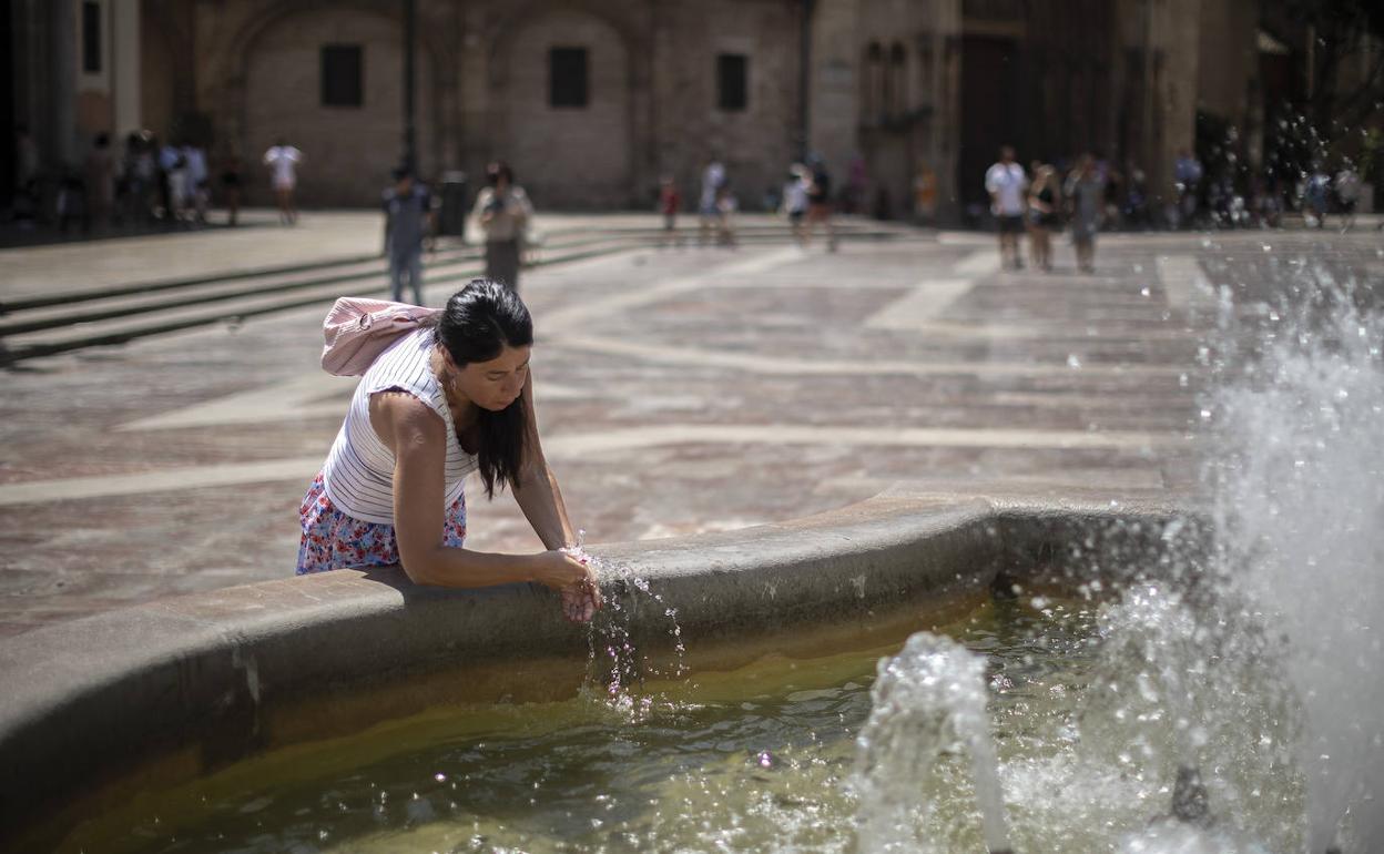 Una joven se refresca en una fuente en Valencia. 