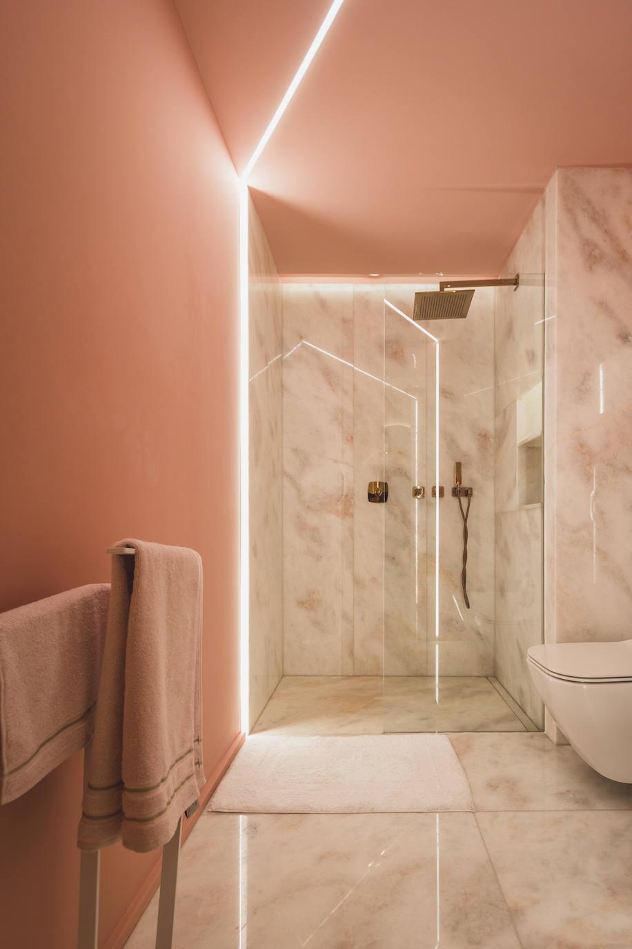 Baño con pavimento y revestimiento de paredes con mármol rosa. Inodoro Forma y grifería Lounge de Porcelanosa.