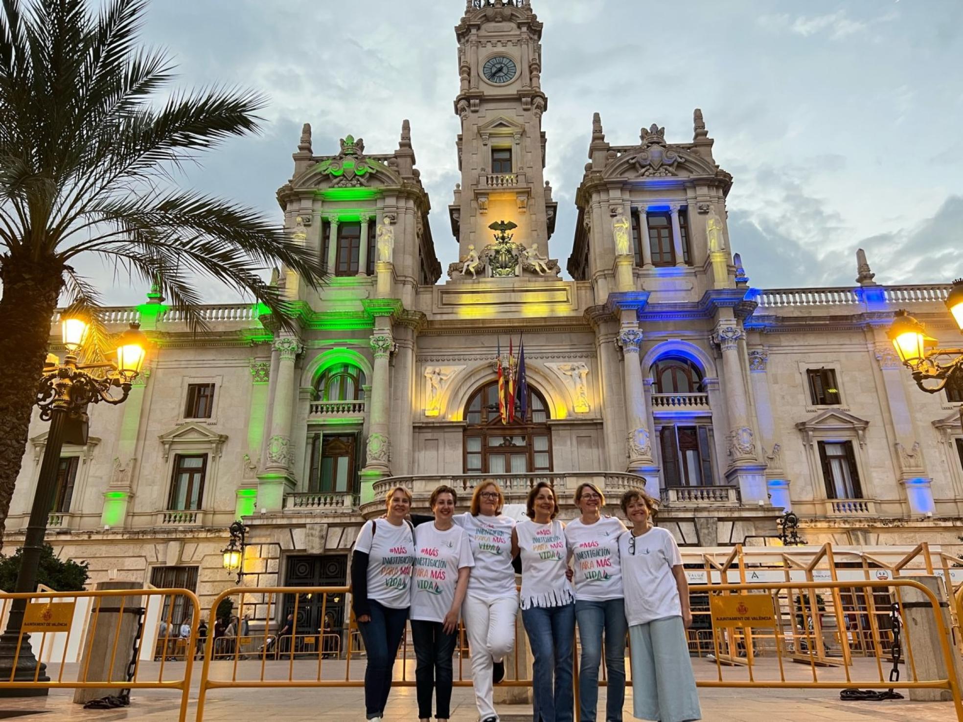 Colores del cáncer. Un grupo de integrantes de la asociación, este miércoles, junto a la fachada iluminada del Ayuntamiento de Valencia. 