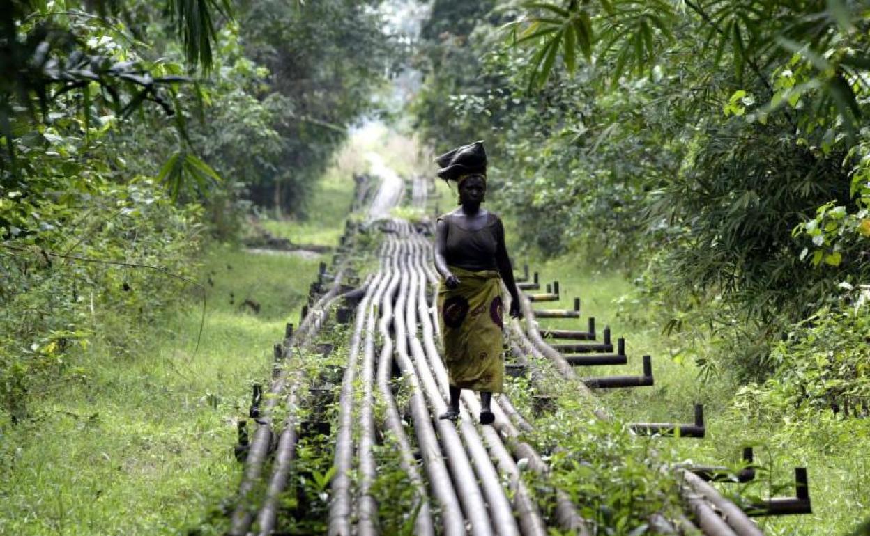 Una mujer camina con un fardo sobre un oleoducto en África. 