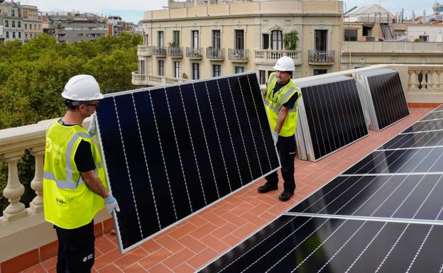 Dos operarios colocan placas solares en una terraza. 