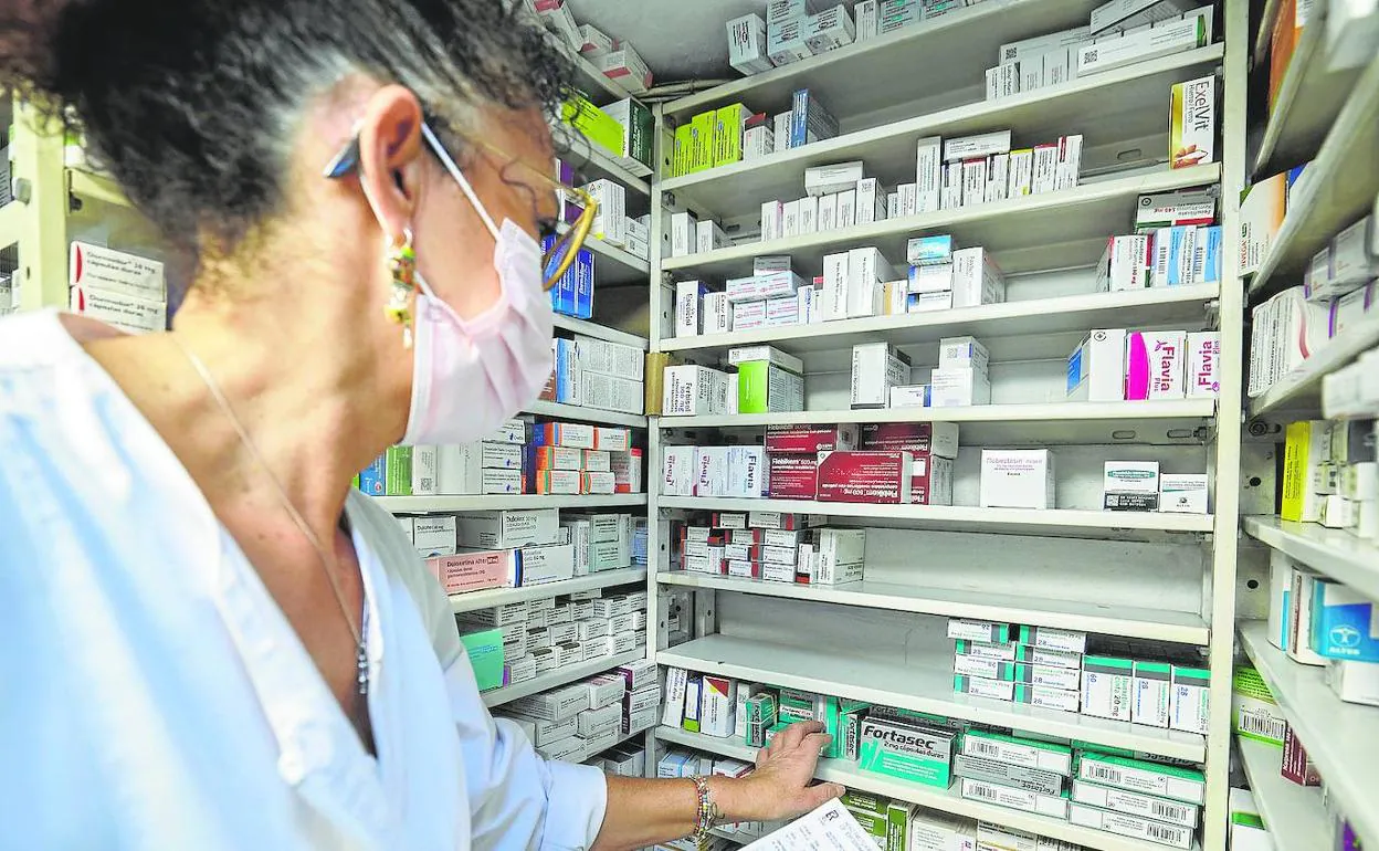 Una profesional muestra los estantes parcialmente vacíos de una farmacia de Valencia.