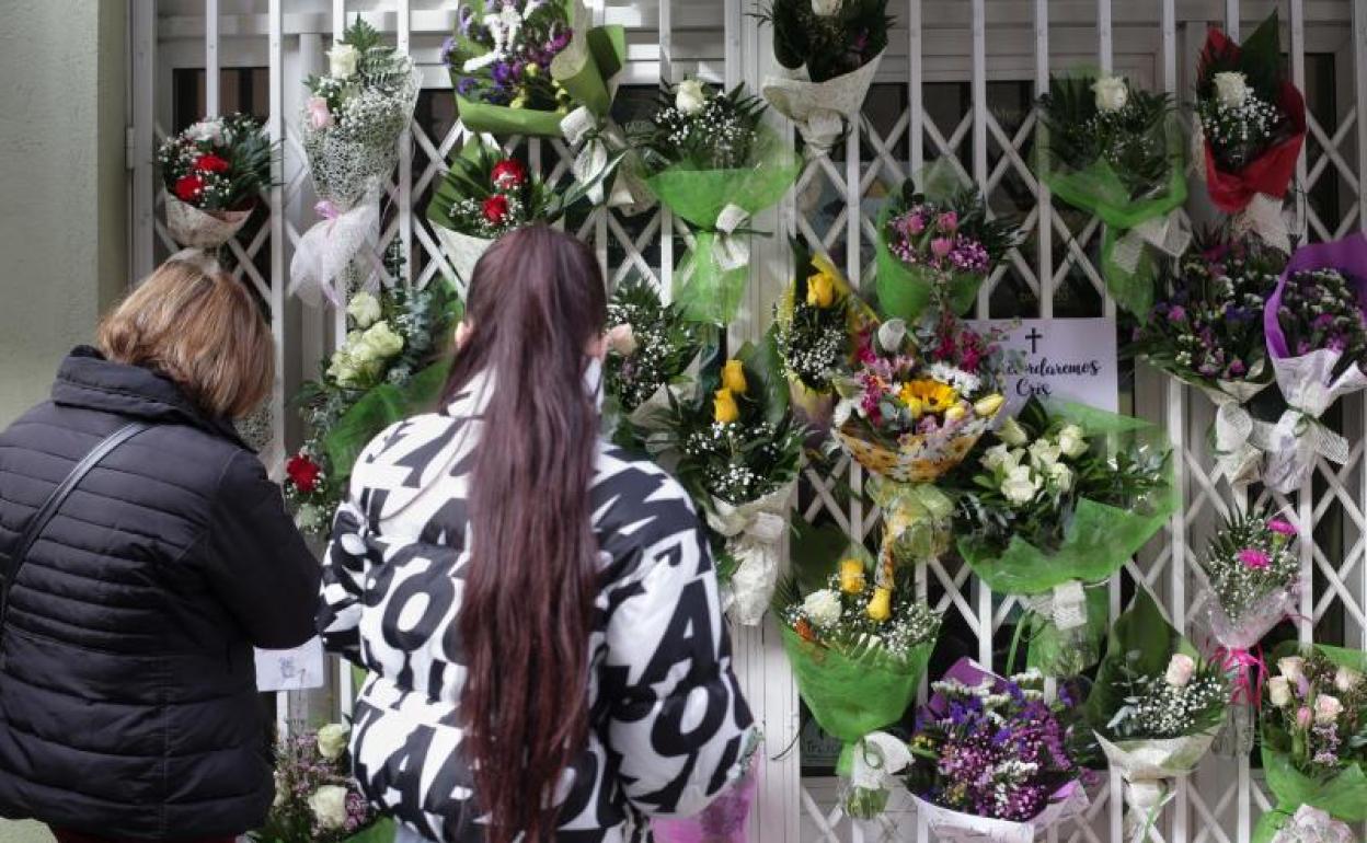 Dos personas observan varias flores colgadas a las puertas de una tienda con motivo del asesinato de la mujer.