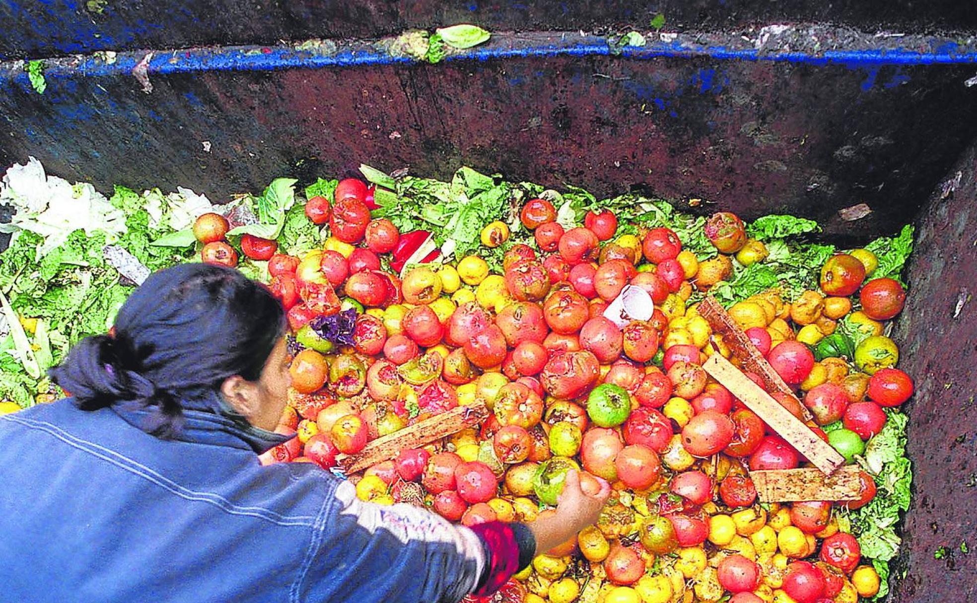 Una mujer recoge alimentos arrojados a un contenedor a las puertas de una gran superficie comercial.