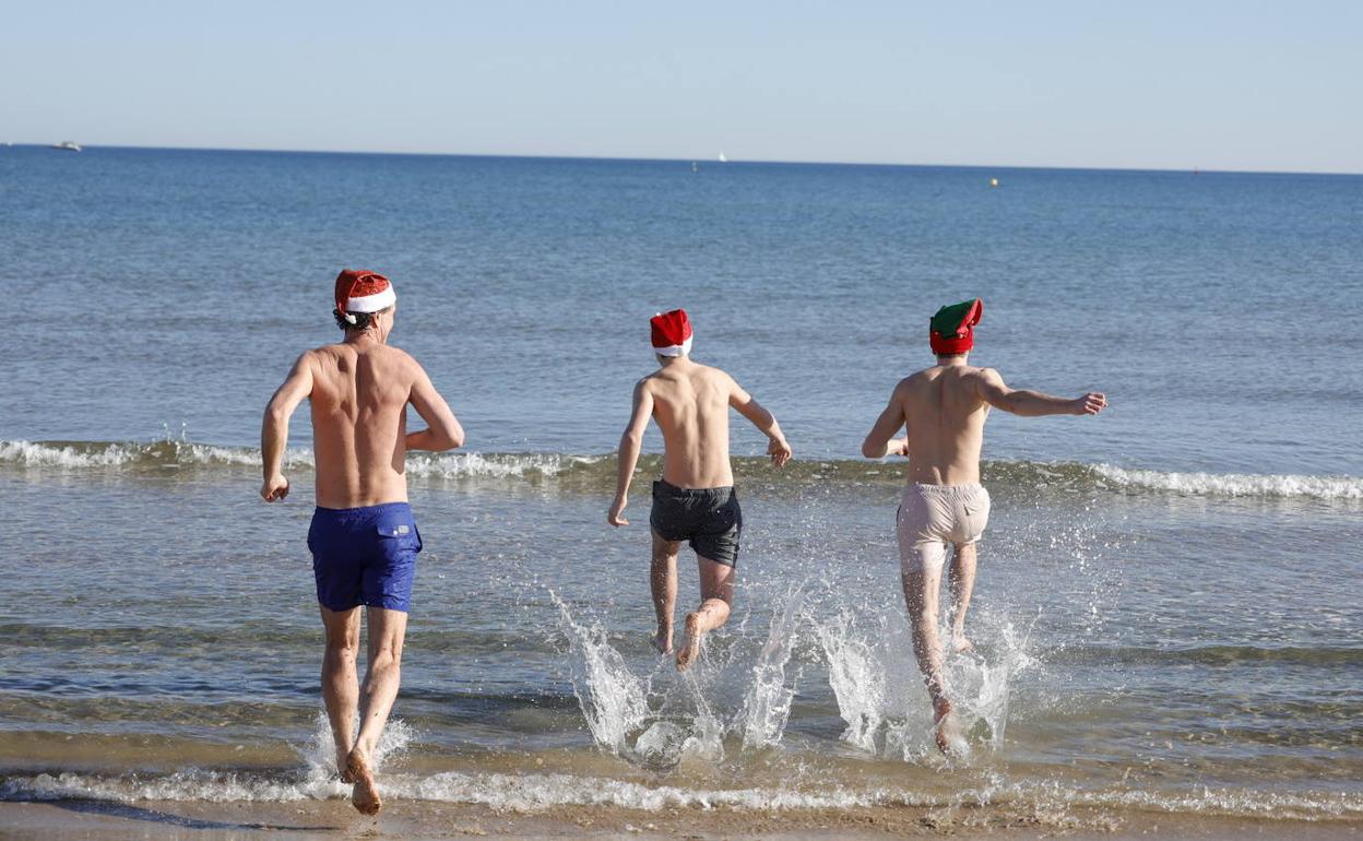 Tres jóvenes se bañan en la playa del Cabanyal, con un gorrito de Papá Noel, en el día de Navidad. 