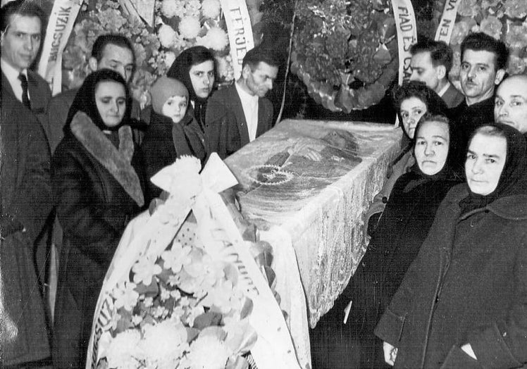 Fotografía del velatorio de un féretro rodeado de coronas de flores.