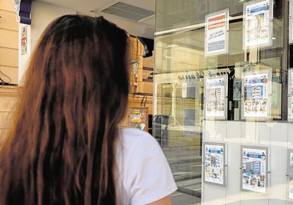 Una joven frente al escaparate de una agencia de alquiler de viviendas.