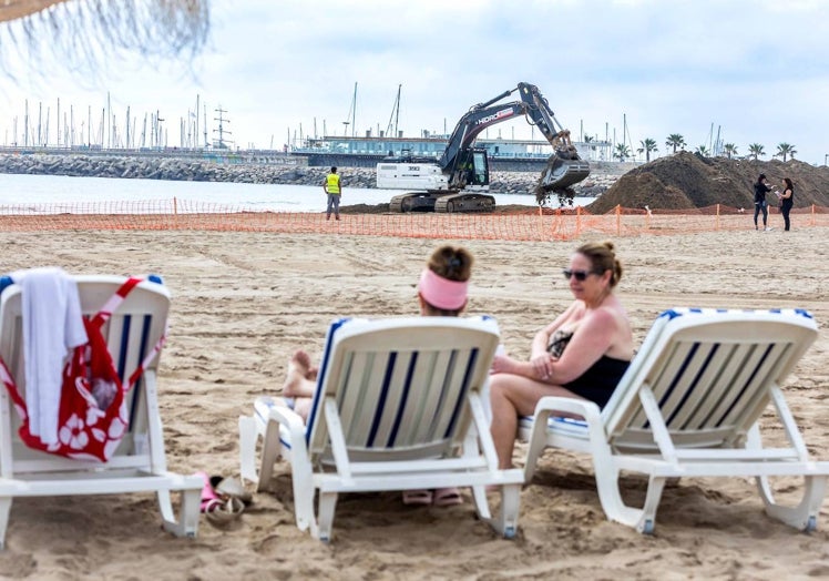 Dos mujeres, sentadas en hamacas, contemplan las montañas de arena de la playa del Cabanyal.