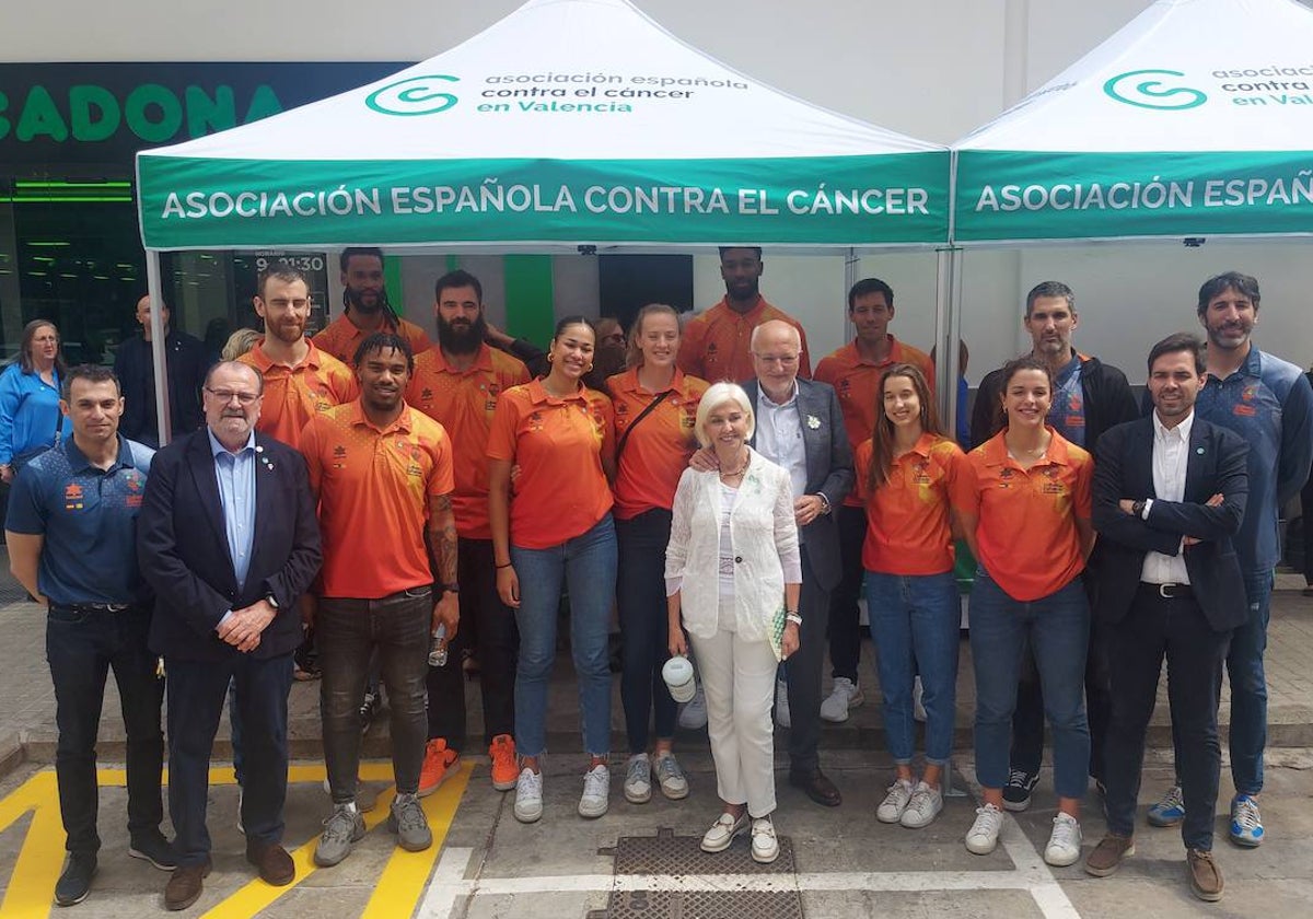 El Valencia Basket posa junto a la mesa petitoria presidida por Hortensia Herrero.