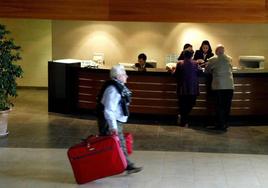 Dos turistas comprueban su reserva en el mostrador de un hotel de Castellón mientras otro recorre el ´hall´ con sus maletas.