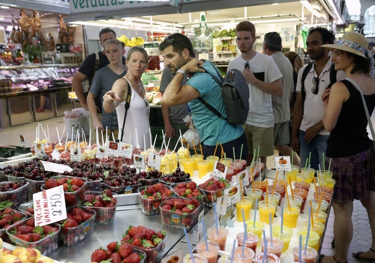 Visitantes en el Mercado Central, junto a un puesto de fruta.