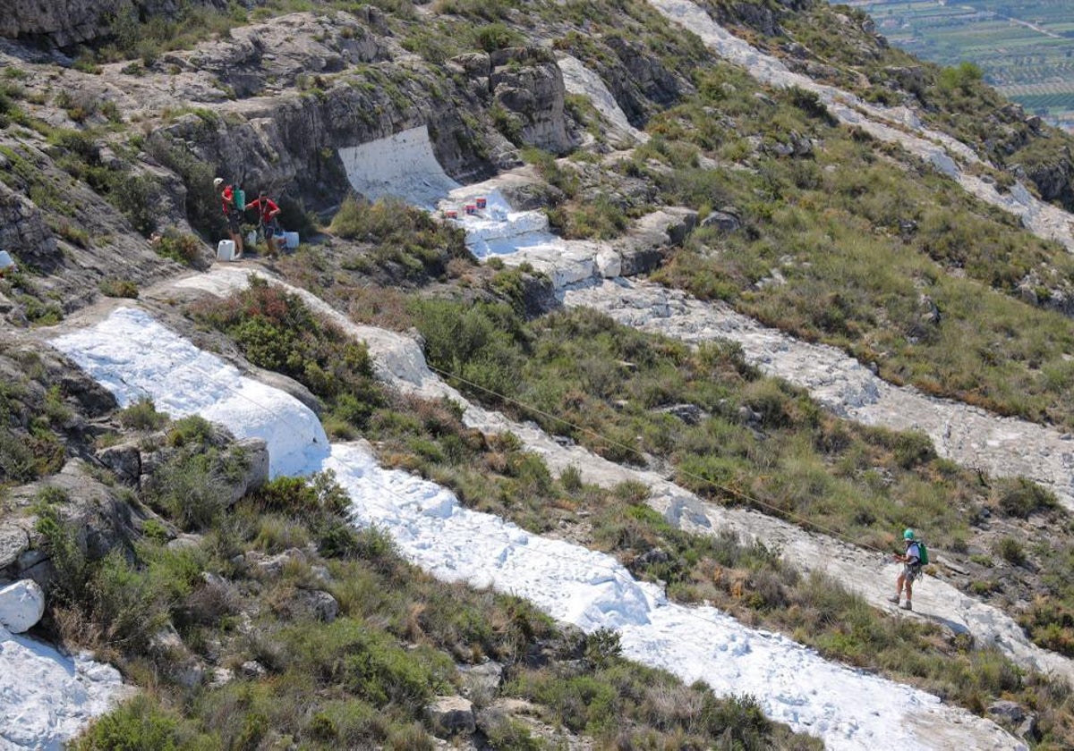 Operarios desbrozando la montaña y repintando las letras en la Serra de Les Raboses de Cullera.