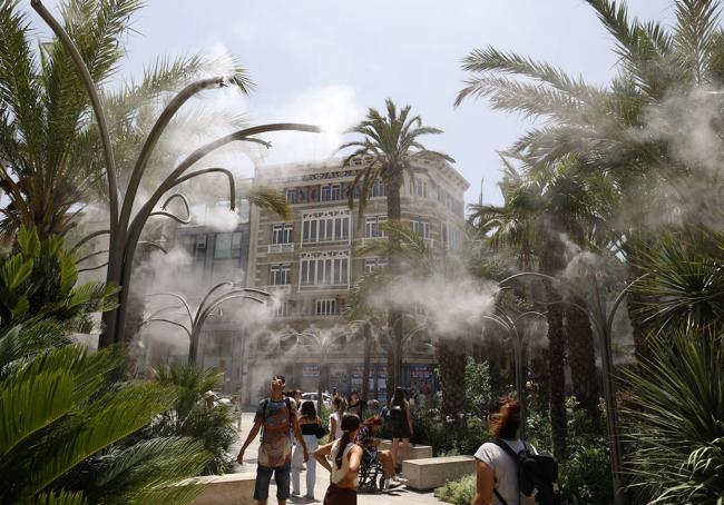 Los aspersores de agua atraen a los paseantes en la plaza de la Reina.