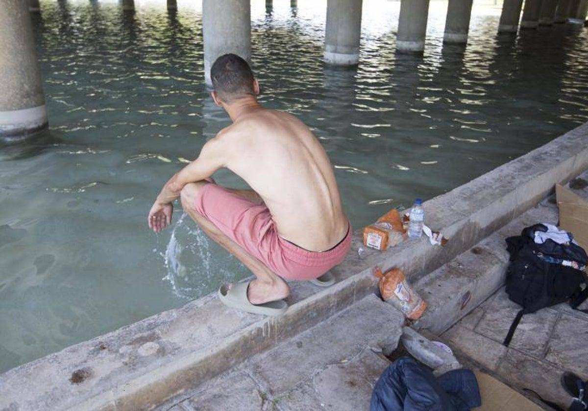 Un indigente se refresca en la fuente del cauce del Turia.