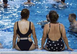 Dos mujeres se refrescan sentadas en el borde de una piscina.