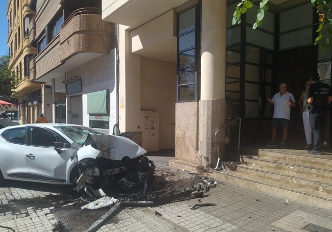 Un policía habla con dos vecinos en la puerta del edificio junto al coche siniestrado.