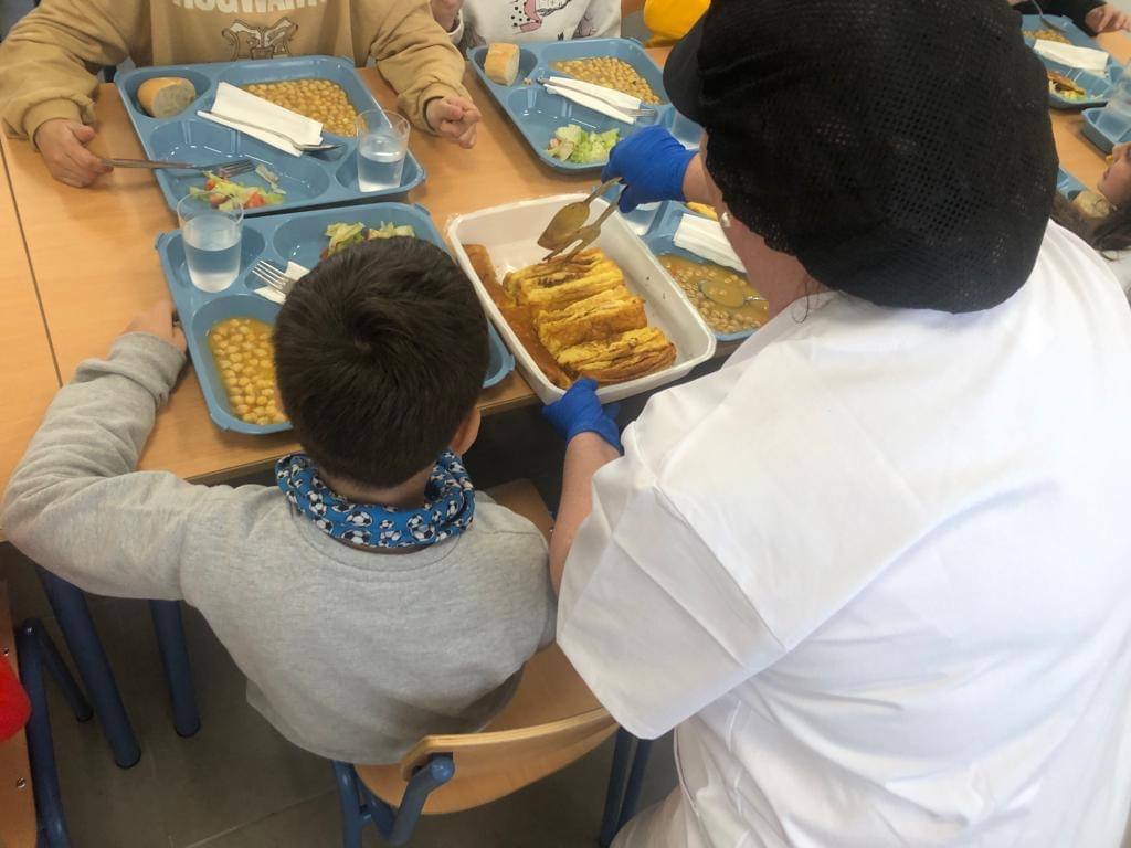 Una cocinera sirve comida en un comedor escolar de la provincia.