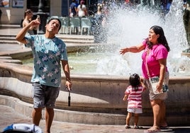 Una familia se refresca junto a una fuente en la plaza de la Virgen.