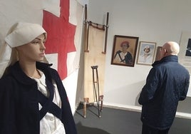 Un maniquí de enfermera junto a una bandera de Cruz Roja y una antigua camilla de campaña, en el arranque de la exposición en Valencia.