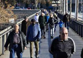 Varias personas caminan abrigadas por una pasarela del río de Valencia.