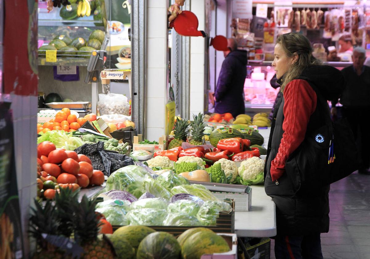 Una mujer, frente a un puesto de frutas y verduras en un mercado.