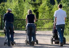 Tres padres pasean a sus hijos por un parque.