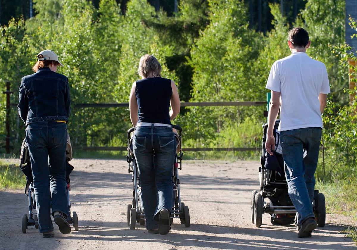 Tres padres pasean a sus hijos por un parque.