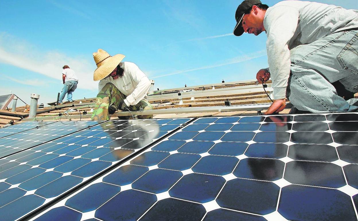 Unos operarios instalan paneles fotovoltaicos sobre el techo de una granja. 