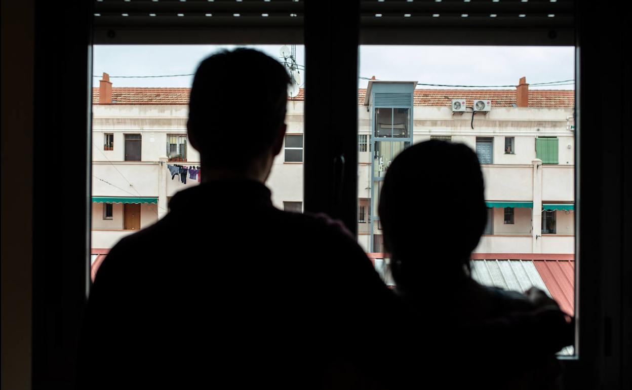 Una pareja mira al horizonte desde la ventana de su casa.