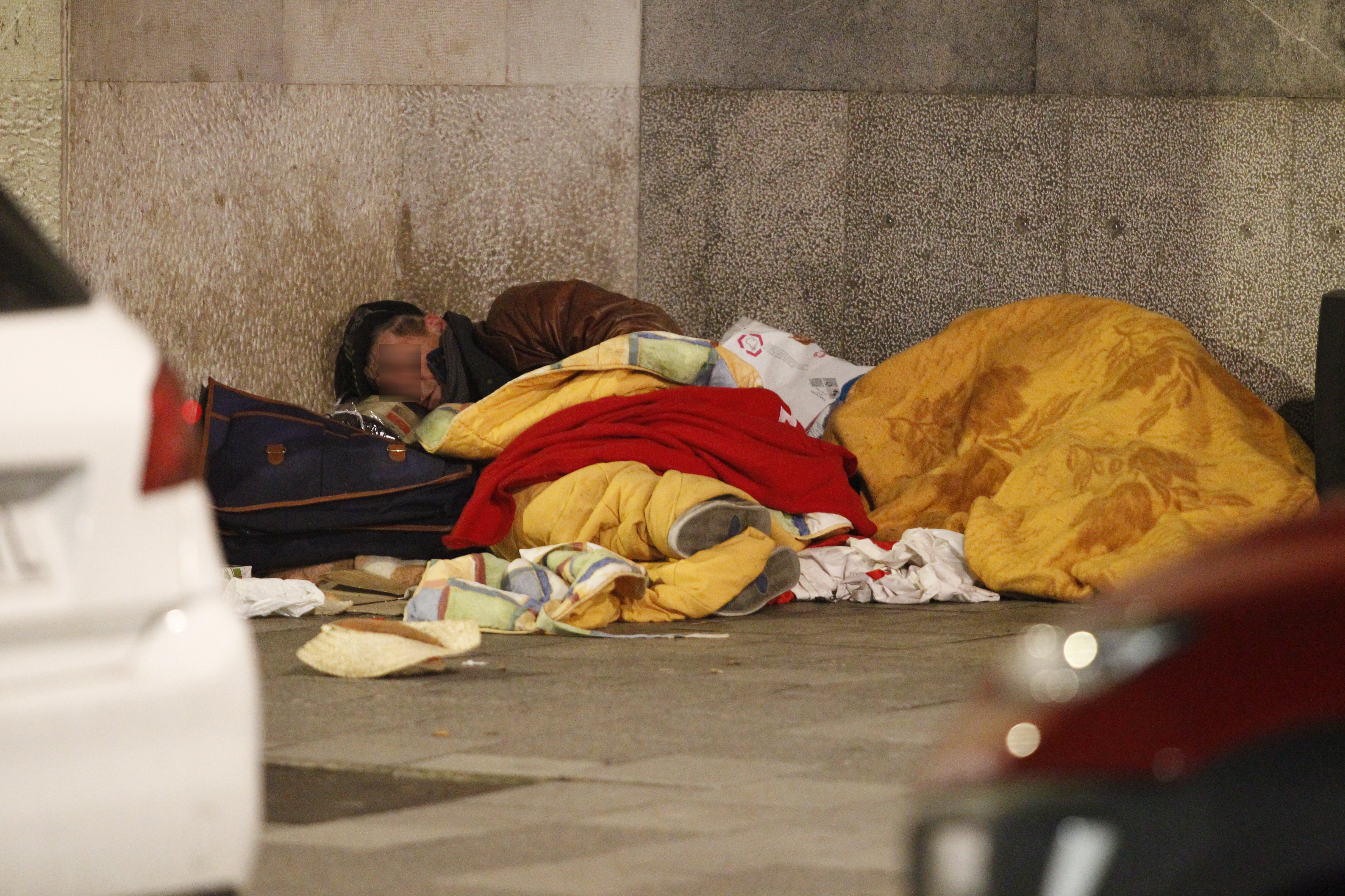 Un hombre sin hogar se camuflka con mantas mientras duerme en la calle.