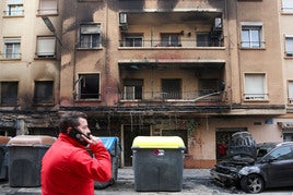 Un hombre habla por el móvil frente al edificio, coches y contenedores calcinados por el incendio de Orriols.