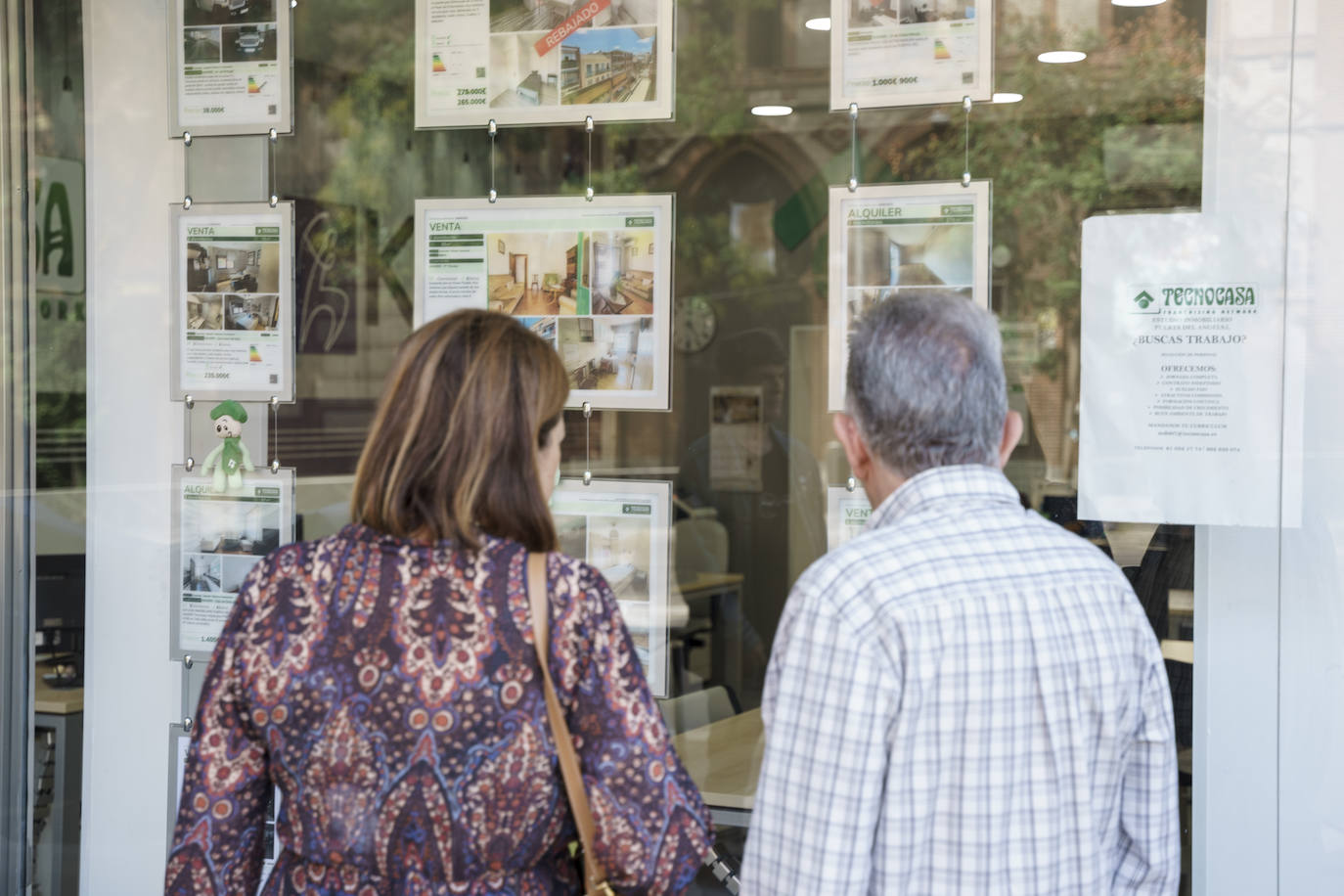 Una pareja mira anuncios de pisos en una inmobiliaria.