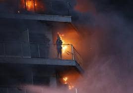 Una persona trata de protegerse de las llamas en una terraza del edificio en llamas.