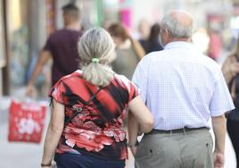 Una pareja de jubilados pasea por una calle comercial.