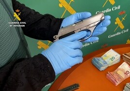 Un agente de la Guardia Civil muestra una de las armas cortas intervenidas al grupo, junto al dinero en efectivo confiscado.