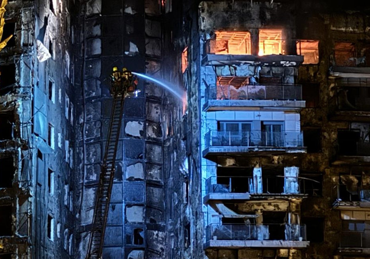 Dos bomberos arrojan agua sobre la fachada del edificio.