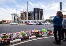 Decenas de velas, muñecos y flores en recuerdo de los fallecidos en el incendio del edificio de Campanar (al fondo).