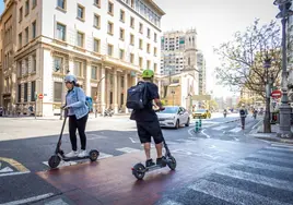 Dos usuarios de patinetes en Valencia por el carril bici.