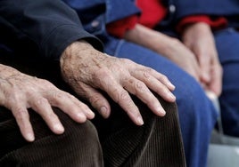 Un anciano posa las manos en las rodillas mientras toma el sol en un parque.