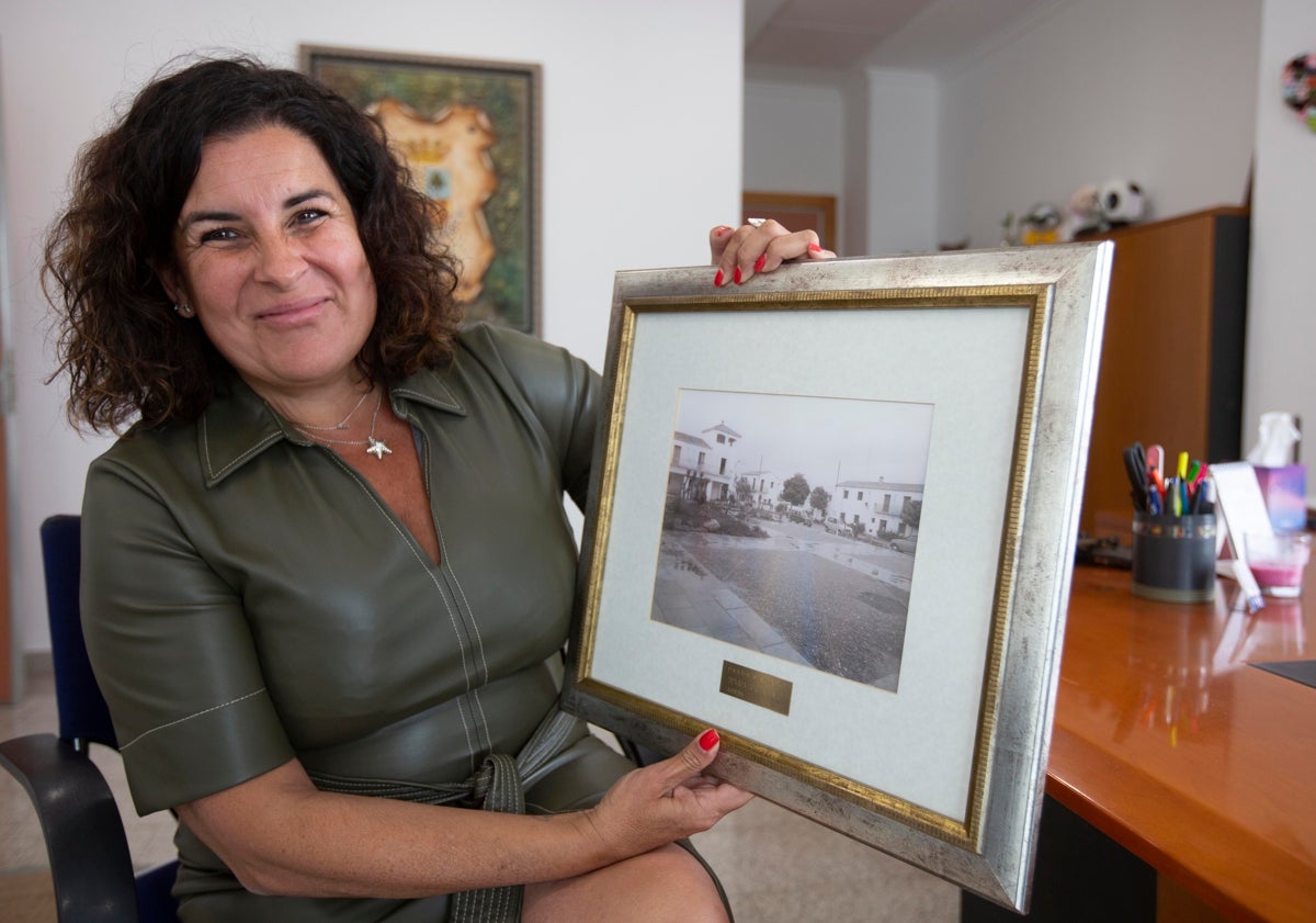 Imagen principal - Eva Tejedor muestra una imagen que recuerda cómo era el aspecto de la plaza del antiguo San Antonio de Benagéber, cuyo ayuntamiento preside; sobre estas líneas, dos fotos en blanco y negro del viejo embalse.