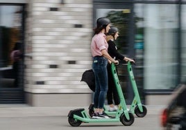 Dos usuarias de patinetes eléctricos, con casco.