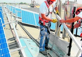 Instaladores de placas fotovoltaicas colocan paneles en el tejado de un almacén.