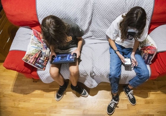 Dos niños con dispositivos digitales en su casa.