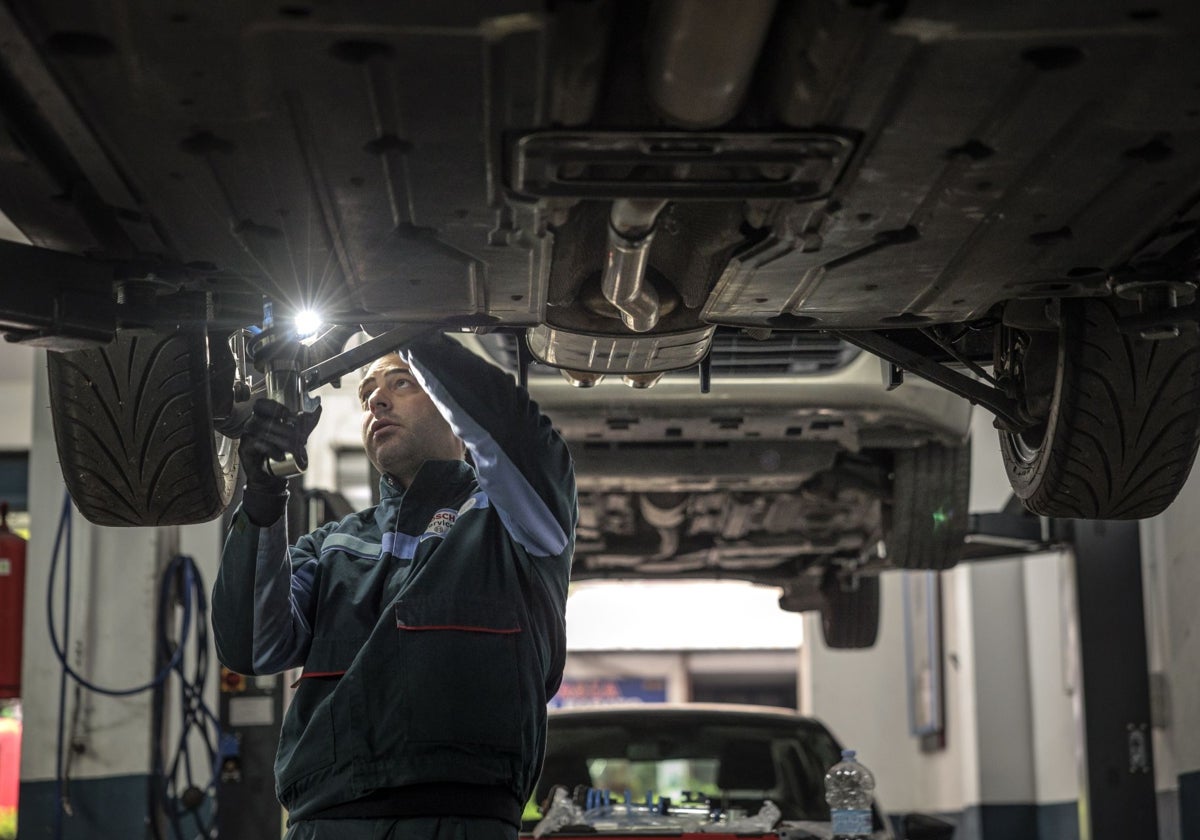 Un trabajador realiza una reparación en la parte inferior de un vehículo.