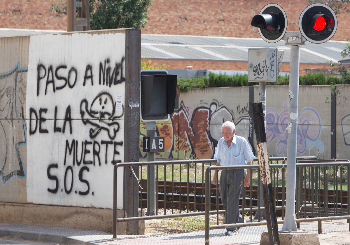 Un vecino cruza el paso a nivel de Alfafar junto a una pintada que alerta de su peligrosidad, esta semana.