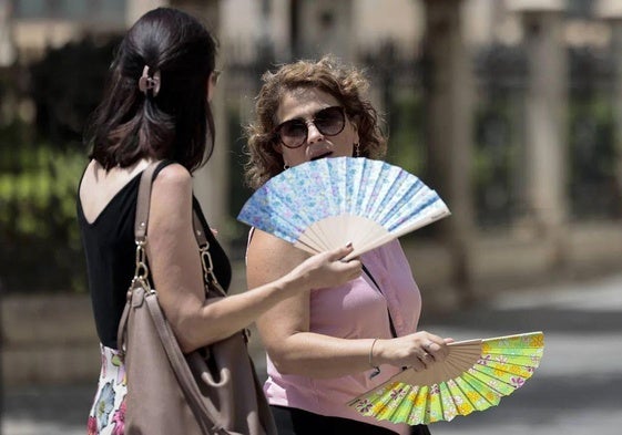 Dos personas combaten con un abanico el calor.