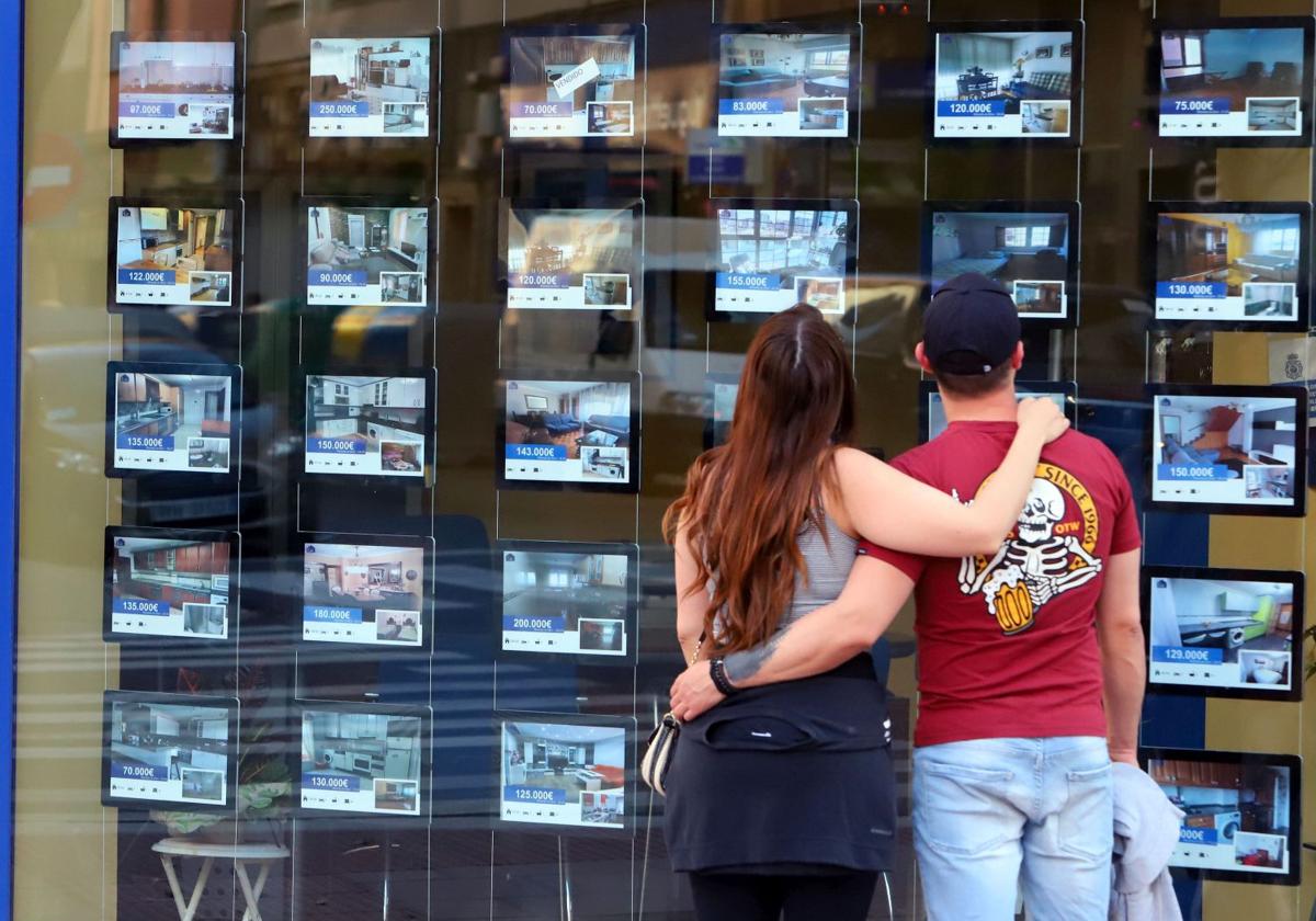 Jovenes mirando escaparates de agencias inmobiliarias.