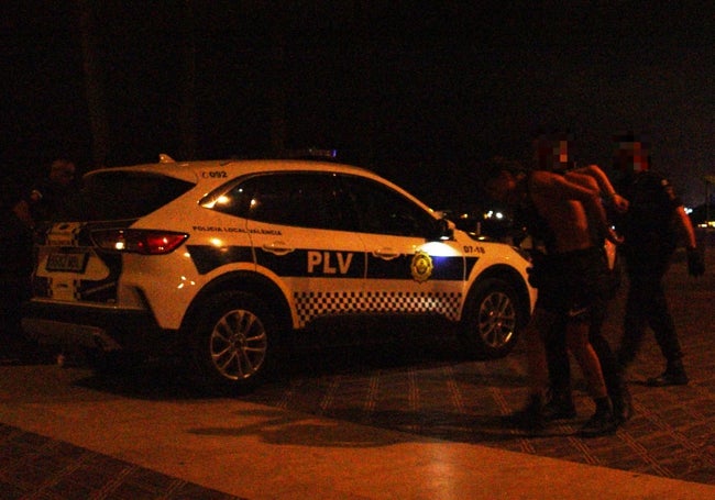 Dos policías locales trasladan a uno de los detenidos al coche patrulla.