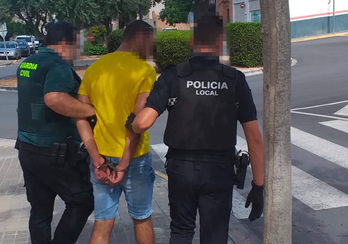 Un guardia civil y un policía trasladan al detenido a un coche patrulla.