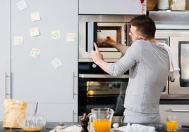 Un hombre calienta comida precocinada en el microondas.